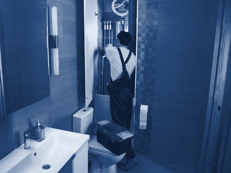 A plumber working behind a bathroom wall